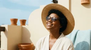 Mulher negra com chapéu de palha de aba larga e óculos de sol em varanda ensolarada